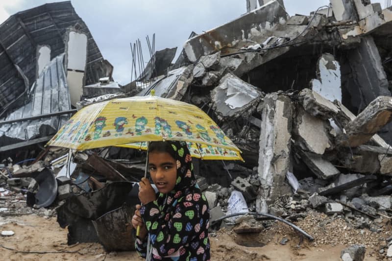 A Palestinian carries an umbrella while waking next to damaged buildings. Abed Rahim Khatib/dpa