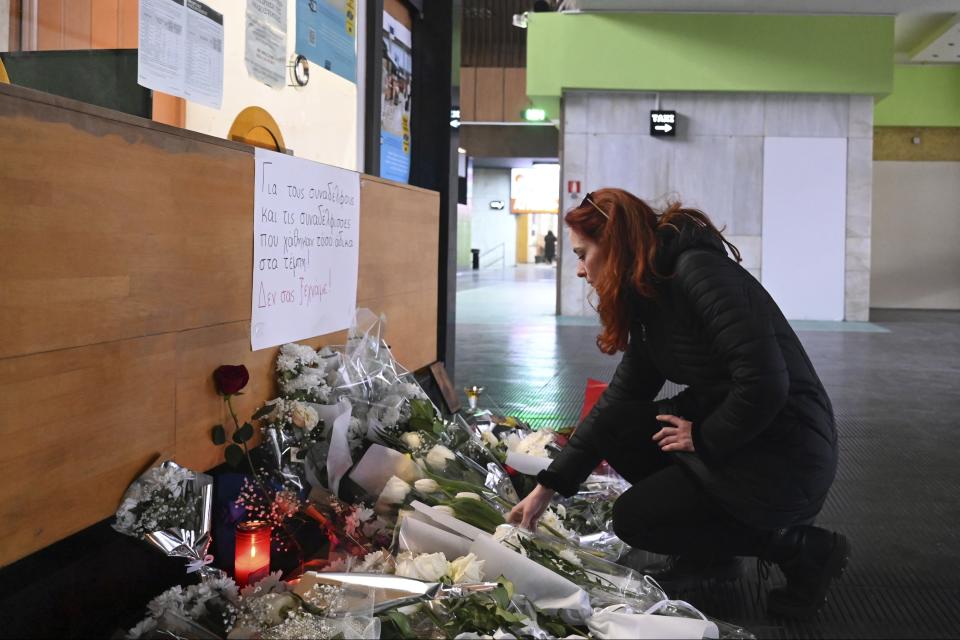A woman lays flowers in memory of the victims of the trains' deadly crash at the train station in the port city of Thessaloniki, northern Greece, Thursday, March 2, 2023. Rescuers using cranes and heavy machinery on Thursday searched the wreckage of trains involved in a deadly collision that sent Greece into national mourning and prompted strikes and protests over rail safety. The sign reads "For the colleagues lost so unfairly at Tempe. We will never forget you." (AP Photo/Giannis Papanikos)