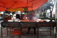 Una mujer utiliza viejos barriles de petróleo como parrilla para cocinar pollos a la brasa en Ciudad México.