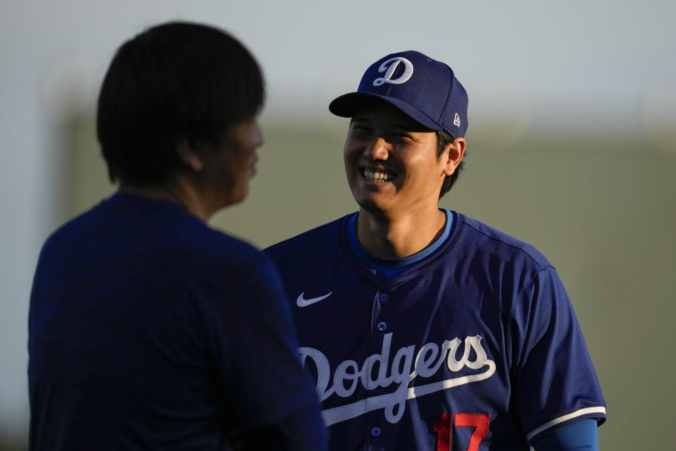 Los Angeles Dodgers designated hitter Shohei Ohtani (17) smiles as he warms up with his interpreter Ippei Mizuhara, left, before a spring training baseball game against the Los Angeles Angels in Phoenix, Tuesday, March 5, 2024. (AP Photo/Ashley Landis)