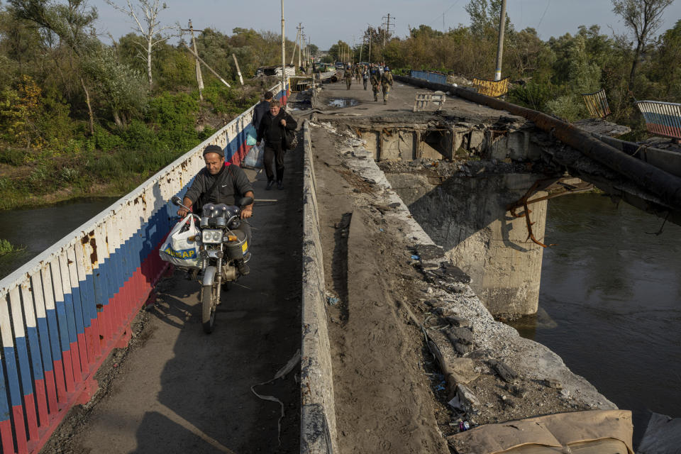 A man drives by motorbike on a destroyed bridge across Oskil river during evacuation in recently liberated town Kupiansk, Ukraine, Saturday, Oct. 1, 2022. (AP Photo/Evgeniy Maloletka)