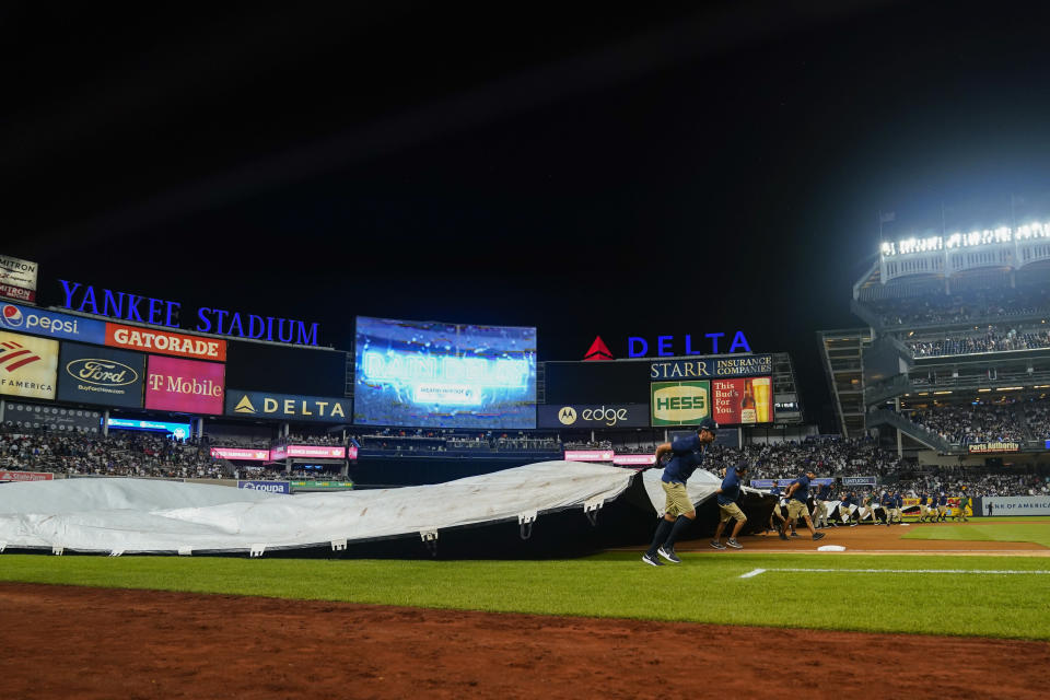 Ground crew members cover the field during a rain delay during the seventh inning of a baseball game between the New York Yankees and the Tampa Bay Rays Wednesday, Aug. 17, 2022, in New York. (AP Photo/Frank Franklin II)