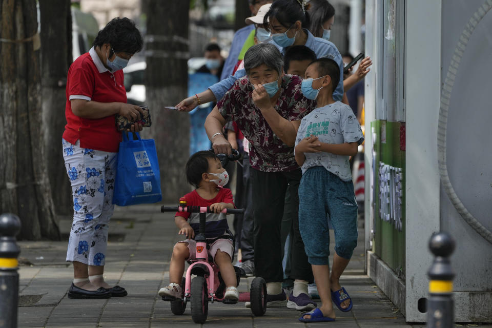 A woman puts on her face mask after getting her routine COVID-19 throat swabs with children at a coronavirus testing site outside a residential complex in Beijing, Monday, Aug. 29, 2022. (AP Photo/Andy Wong)