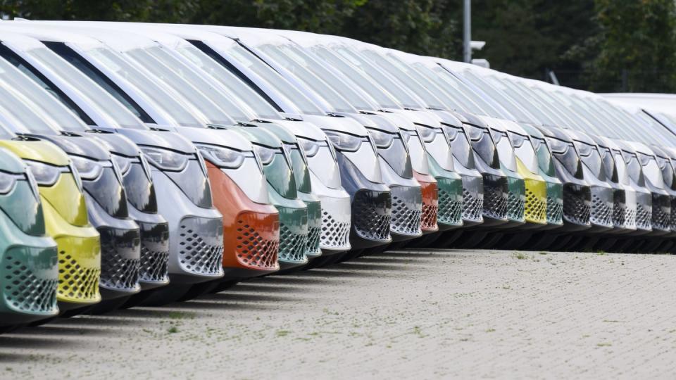 a row of vw id buzz vans of different colors sits in a factory parking lot
