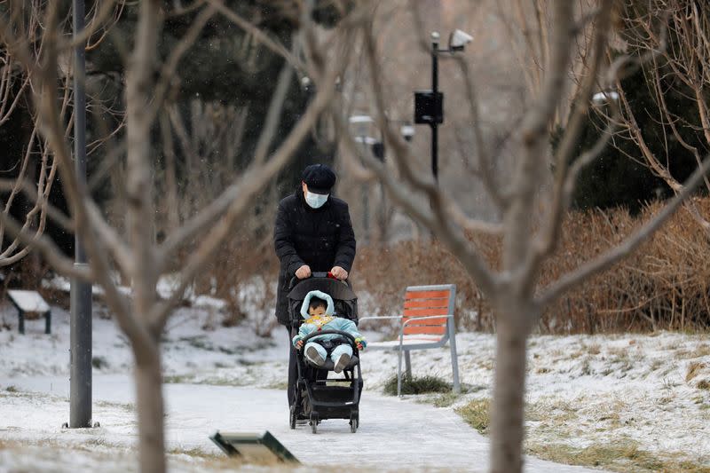 A person wearing a face mask following the coronavirus disease (COVID-19) outbreak, pushes a child in a pram on a snowy day in Beijing, China