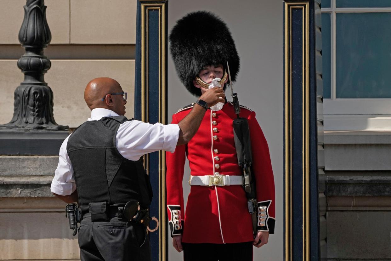 Police officer givers water to a British soldier wearing a traditional bearskin hat, on guard duty outside Buckingham Palace, during hot weather in London, . The British government have issued their first-ever "red" warning for extreme heat. The alert covers large parts of England on Monday and Tuesday, when temperatures may reach 40 degrees Celsius (104 Fahrenheit) for the first time, posing a risk of serious illness and even death among healthy people, the U.K. Met Office, the country's weather service, said Friday Heat, London, United Kingdom - 18 Jul 2022