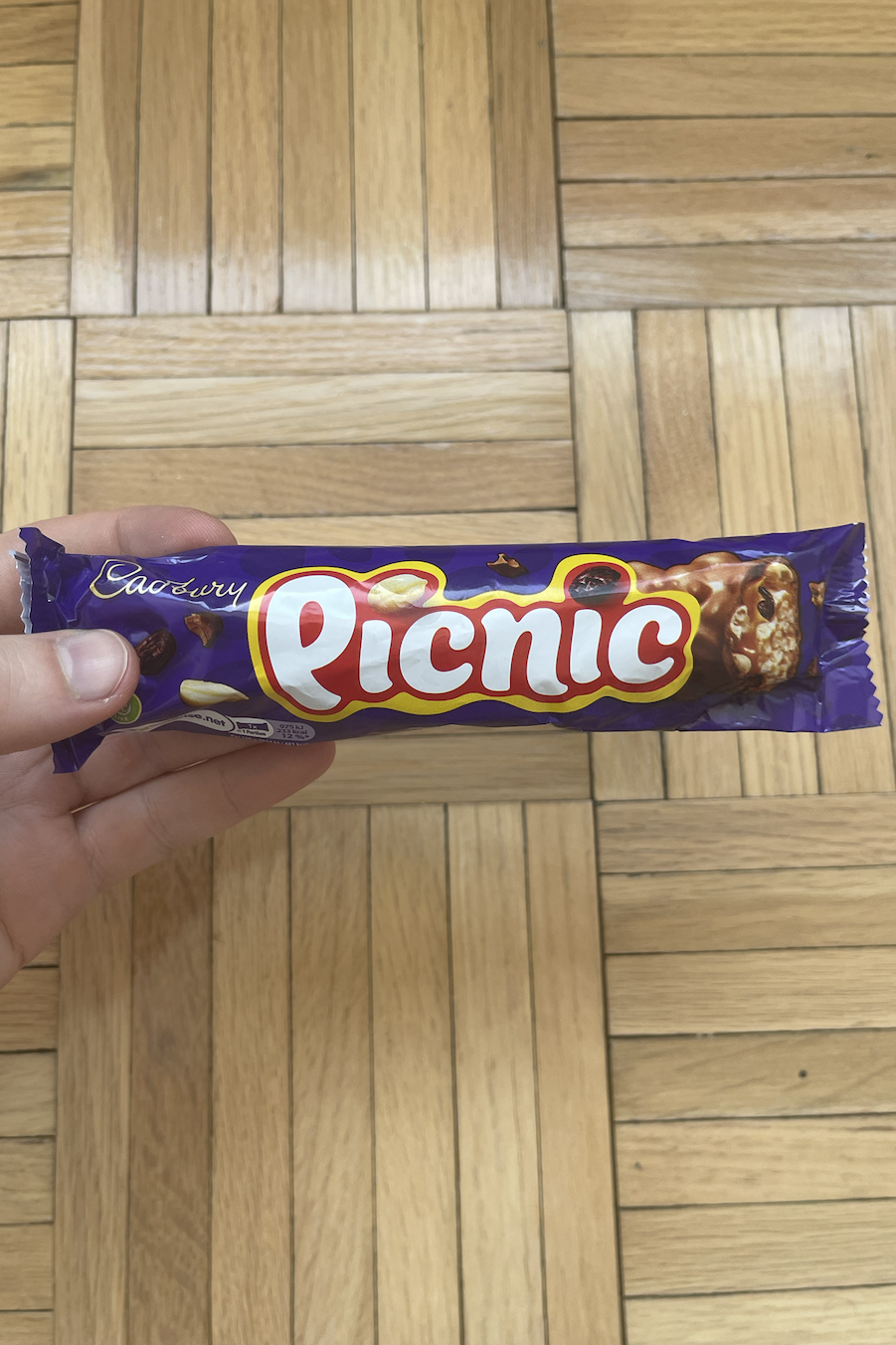 Hand holding a Cadbury Picnic chocolate bar over wooden floor