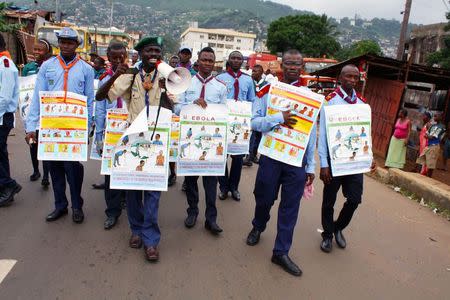 Members of a UNICEF-supported social mobilization team walk on a street, carrying posters with information on the symptoms of Ebola and best practices to help prevent its spread, in Freetown, Sierra Leone, in this handout photo courtesy of UNICEF taken in August 2014. REUTERS/Issa Davies/UNICEF/Handout via Reuters