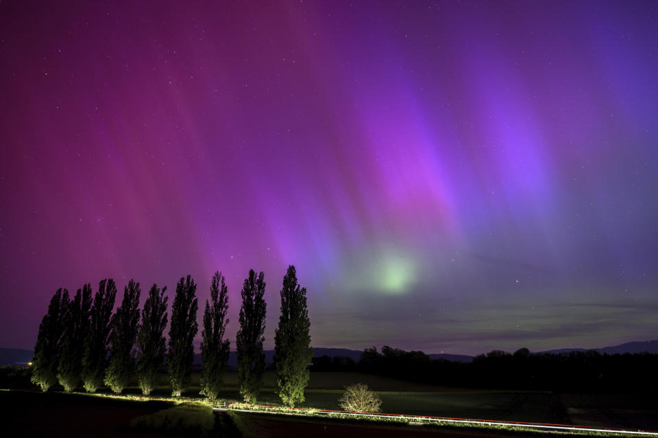 En esta fotografía de larga exposición, un auto circula por una carretera mientras las auroras boreales iluminan el cielo nocturno en Daillens, Suiza, el 11 de mayo de 2024. (Laurent Gillieron/Keystone vía AP)