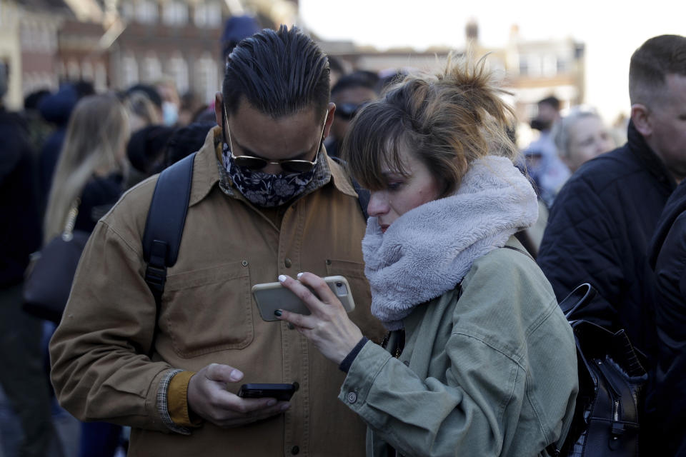 People watch live coverage on a phone outside Windsor Castle during the funeral of Britain's Prince Philip in Windsor, England, Saturday, April 17, 2021. Philip died April 9 at the age of 99 after 73 years of marriage to Britain's Queen Elizabeth II. Coronavirus restrictions mean there will be only 30 mourners for the service, including the widowed queen, her four children and her eight grandchildren. (AP Photo/Matt Dunham)