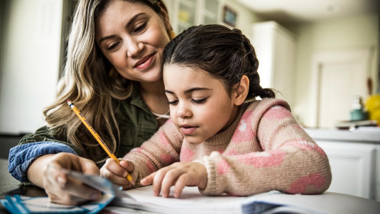  Mother and daughter (7 years) doing homework at table. 