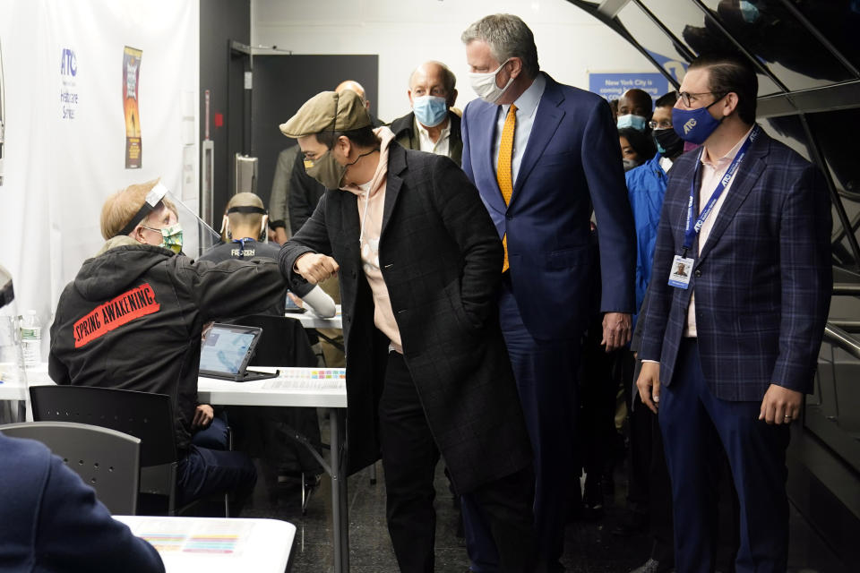 Actor Lin-Manuel Miranda, second left, greets a vaccination site worker, left, as he and New York Mayor Bill de Blasio, third left, tour the grand opening of a Broadway COVID-19 vaccination site intended to jump-start the city's entertainment industry, in New York, Monday, April 12, 2021. (AP Photo/Richard Drew, Pool)