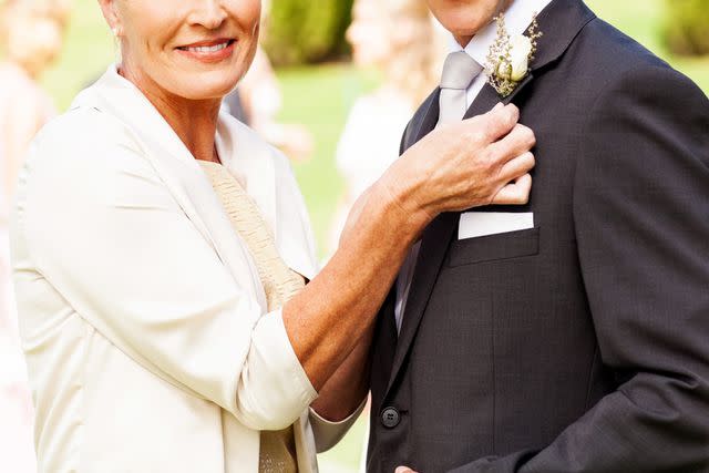 <p>Getty</p> Portrait of happy mother pinning corsage on groom's suit at outdoor wedding