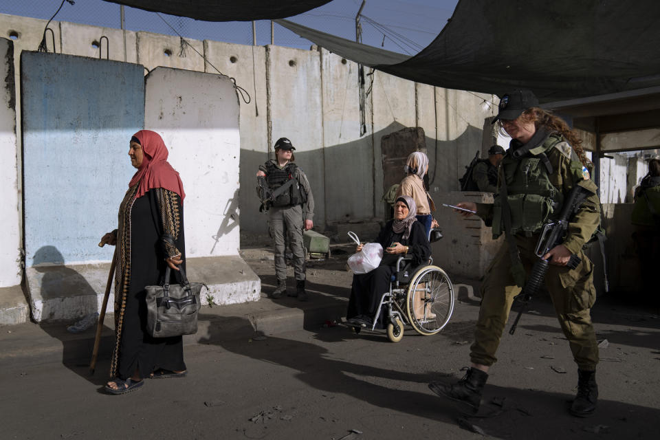 FILE - Palestinian women walk past a section of Israel's separation barrier to pray at the Al-Aqsa Mosque in Jerusalem on the fourth Friday of the Muslim holy month of Ramadan at the Qalandia checkpoint between the West Bank city of Ramallah and Jerusalem, Friday, April 29, 2022. The Israeli military body in charge of civilian affairs in the occupied West Bank has developed a new policy that would heavily regulate entry into the territory. (AP Photo/Oded Balilty, File)