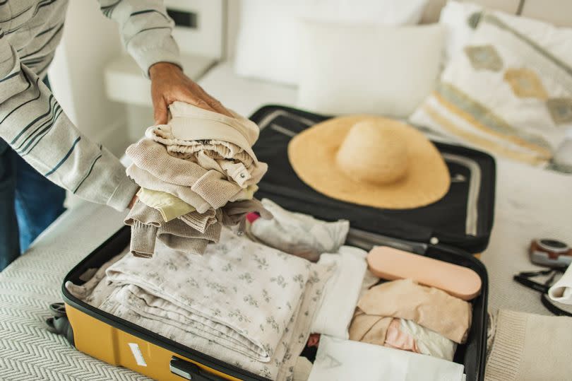 Happy family with mother and toddler blond girl, grandfather and grandmother packing clothes in huge yellow luggage on bed. Getting ready for a vacation. Travellers accessories. Travel and vacation concept.