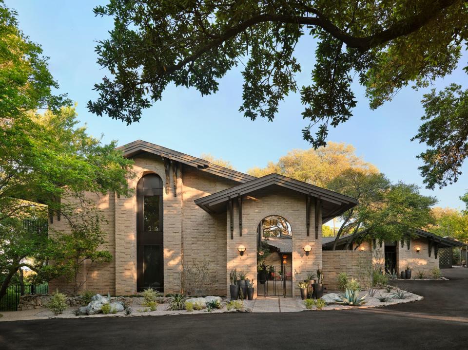 A lake house with tan bricks surrounded by trees.