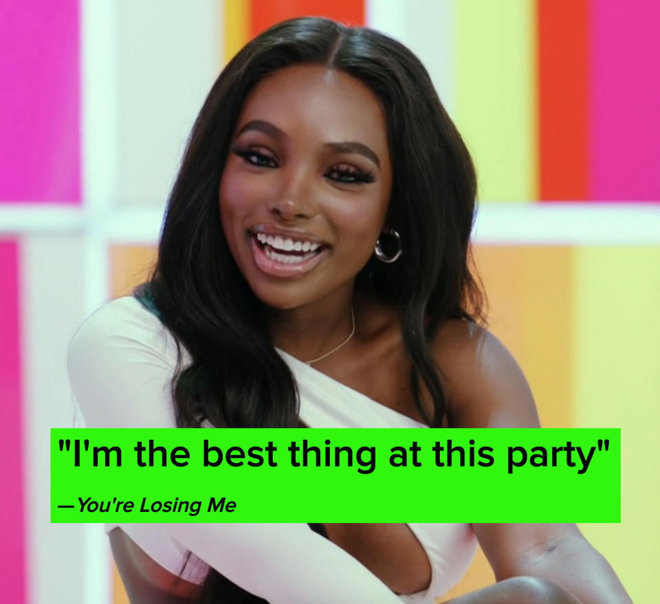 A smiling JaNa wearing a unique off-shoulder top with cut-out design, seated in front of a colorful background