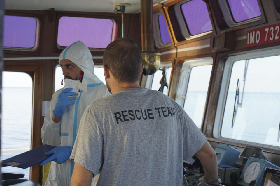 A Ministry of Health worker speaks with a crew member of the Open Arms Spanish humanitarian boat off the coast of the Sicilian island of Lampedusa, southern Italy, Sunday, Aug.18, 2019. (AP Photo/Francisco Gentico)