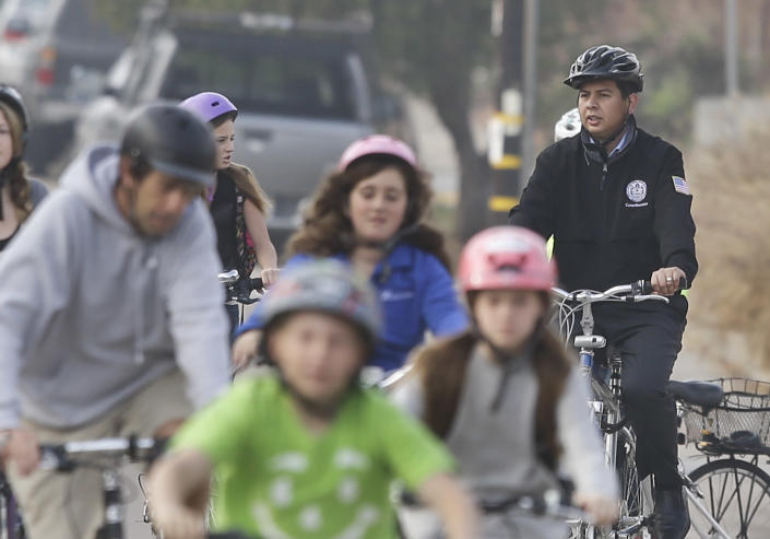 In a Thursday, Jan. 30, 2014 photo, San Diego Mayoral candidate David Alvarez, right, rides through traffic with children and parents headed to school, in San Diego. Alvarez finished second in a first round of voting by winning south of the freeway in predominantly Latino areas. Republican Councilman Kevin Faulconer easily topped a field of 11 candidates in a first round of voting by dominating in wealthier neighborhoods north of the freeway. (AP Photo/Lenny Ignelzi)