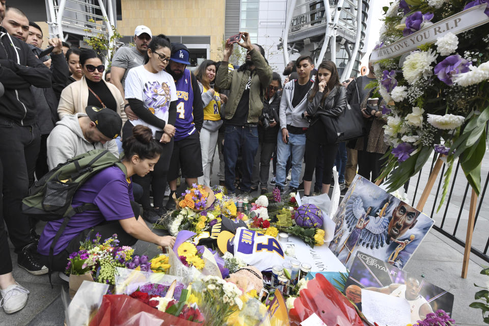 Valerie Samano, left, places flowers at a memorial near Staples Center after the death of Laker legend Kobe Bryant Sunday, Jan. 26, 2020, in Los Angeles. (AP Photo/Michael Owen Baker)