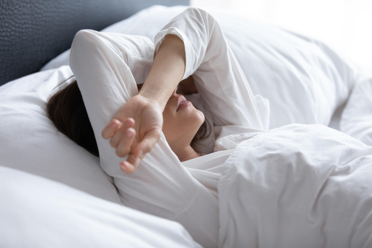 Sleepless young woman suffering from insomnia or nightmares close up, bad dreams, tired depressed female covering eyes with hands, lying on pillow in bed, feeling headache or migraine