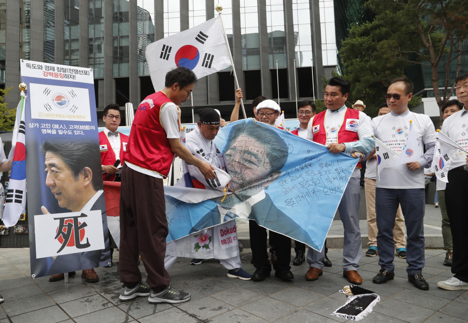 A South Korean protester uses scissors to cut an image of Japanese Prime Minister Shinzo Abe during a rally denouncing the Japanese government's decision on their exports to South Korea in front of the Japanese Embassy in Seoul, South Korea, Tuesday, July 23, 2019. The signs read "Punish economic aggression." (AP Photo/Ahn Young-joon)