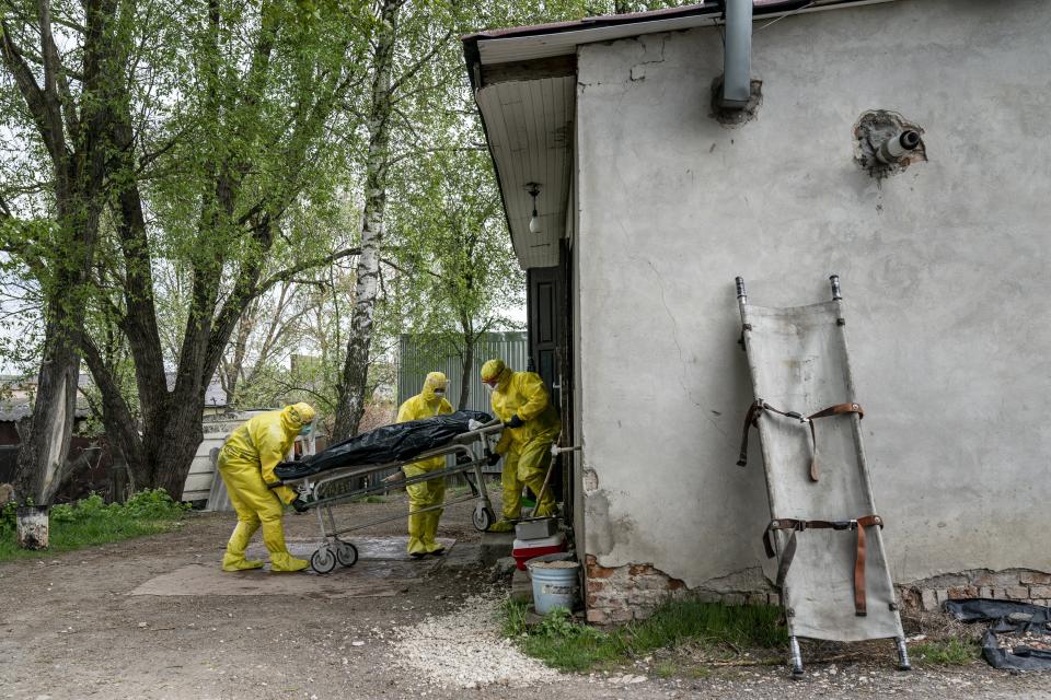 In this photo taken on Thursday, April 30, 2020, pathologists wearing special suits to protect against coronavirus, transport the body of a man who died of coronavirus, at the doors of the morgue in Ternopil, Ukraine. Ukraine's troubled health care system has been overwhelmed by COVID-19, even though it has reported a relatively low number of cases. (AP Photo/Evgeniy Maloletka)