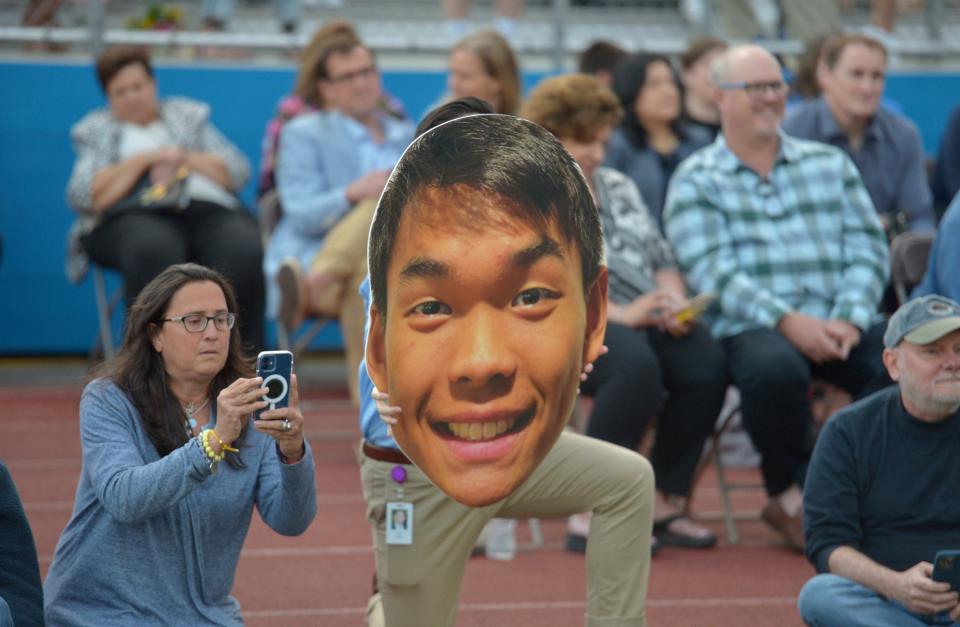 Ryan Kwan holds a fathead cutout of his brother, graduate Zachary Kwan, during Natick High School Graduation at Memorial Field, June 3, 2022.