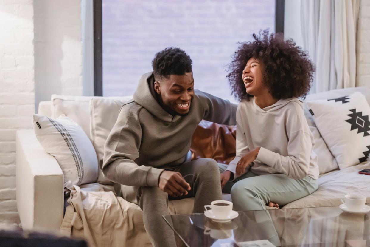 black woman and black man sitting on couch laughing in sweatsuits