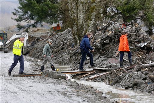 Workers use bits of plywood to cross over a small stream of muddy water flowing from the the west side of the mudslide on Highway 530 near mile marker 37  in Arlington, Wash., on Sunday, March 30, 2014. Periods of rain and wind have hampered efforts the past two days, with some rain showers continuing today. Last night, the confirmed fatalities list was updated to 18, with the number of those missing falling from 90 to 30. (AP Photo/Rick Wilking, Pool)