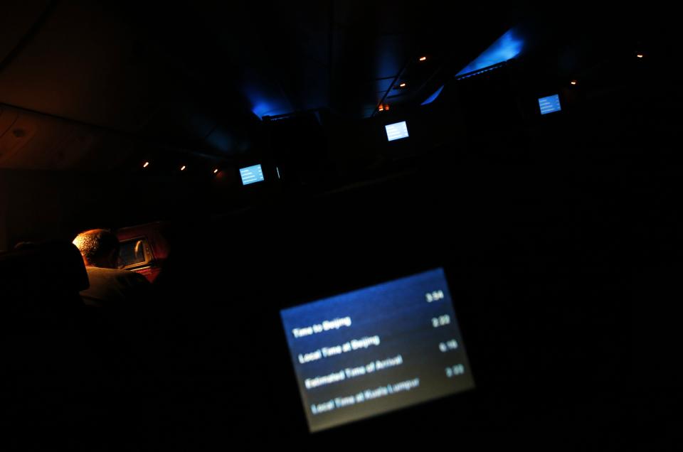 A passenger, John Gardner of Australia, focuses on his Sudoku puzzle, as other passengers sleep onboard Malaysia Airlines Boeing 777-200ER flight MH318 as it cruises towards Beijing