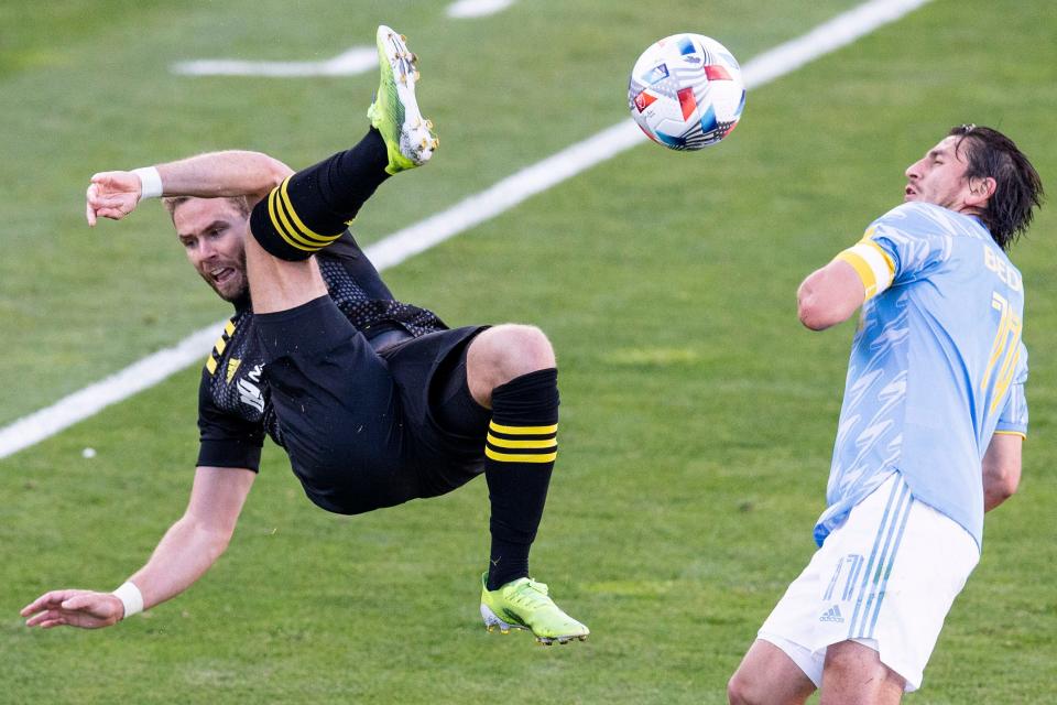 Columbus Crew defender Josh Williams (left) clears the ball out of his own end with a bicycle kick in front of the Philadelphia Union's Alejandro Bedoya.