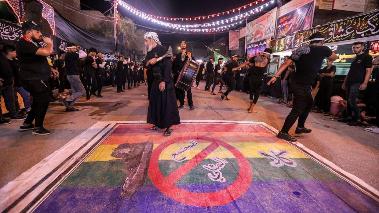 Shiite Muslim devotees self-flagellate over an unfurled banner on the ground depicting the Pride rainbow flag defaced with a boot and the Arabic slogan 