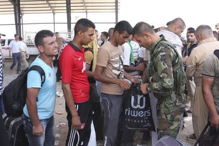 An Iraqi-Kurdish security personnel conducts a search through belongings, as families fleeing the violence in the Iraqi city of Mosul, wait at a checkpoint in the outskirts of Arbil, in Iraq's Kurdistan region, June 10, 2014. REUTERS/Azad Lashkari