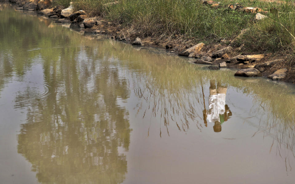 Kalmane Kamegowda, a 72-year-old shepherd, is reflected in a pond he created at a hillock near Dasanadoddi village, 120 kilometers (75 miles) west of Bengaluru, India, Wednesday, Nov. 25, 2020. Kamegowda, who never attended school, says he's spent at least $14,000 from his and his son’s earnings, mainly through selling sheep he tended over the years, to dig a chain of 16 ponds on a picturesque hill near his village. (AP Photo/Aijaz Rahi)