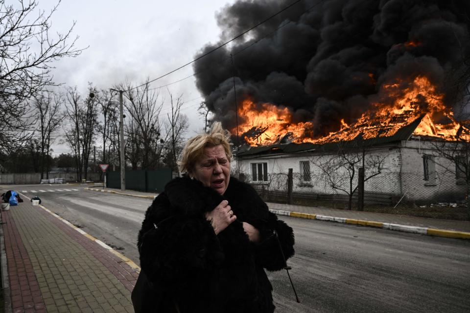 A woman reacts as she stands in front of a burning house 