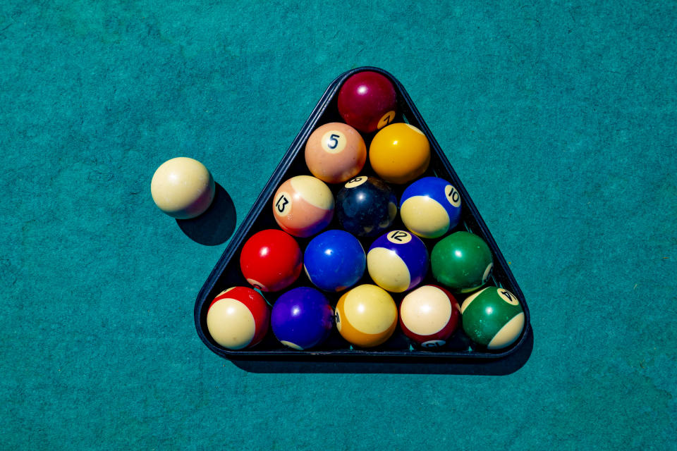 A set of billiard balls arranged in a triangle, ready for a game, with one white cue ball positioned outside the triangle