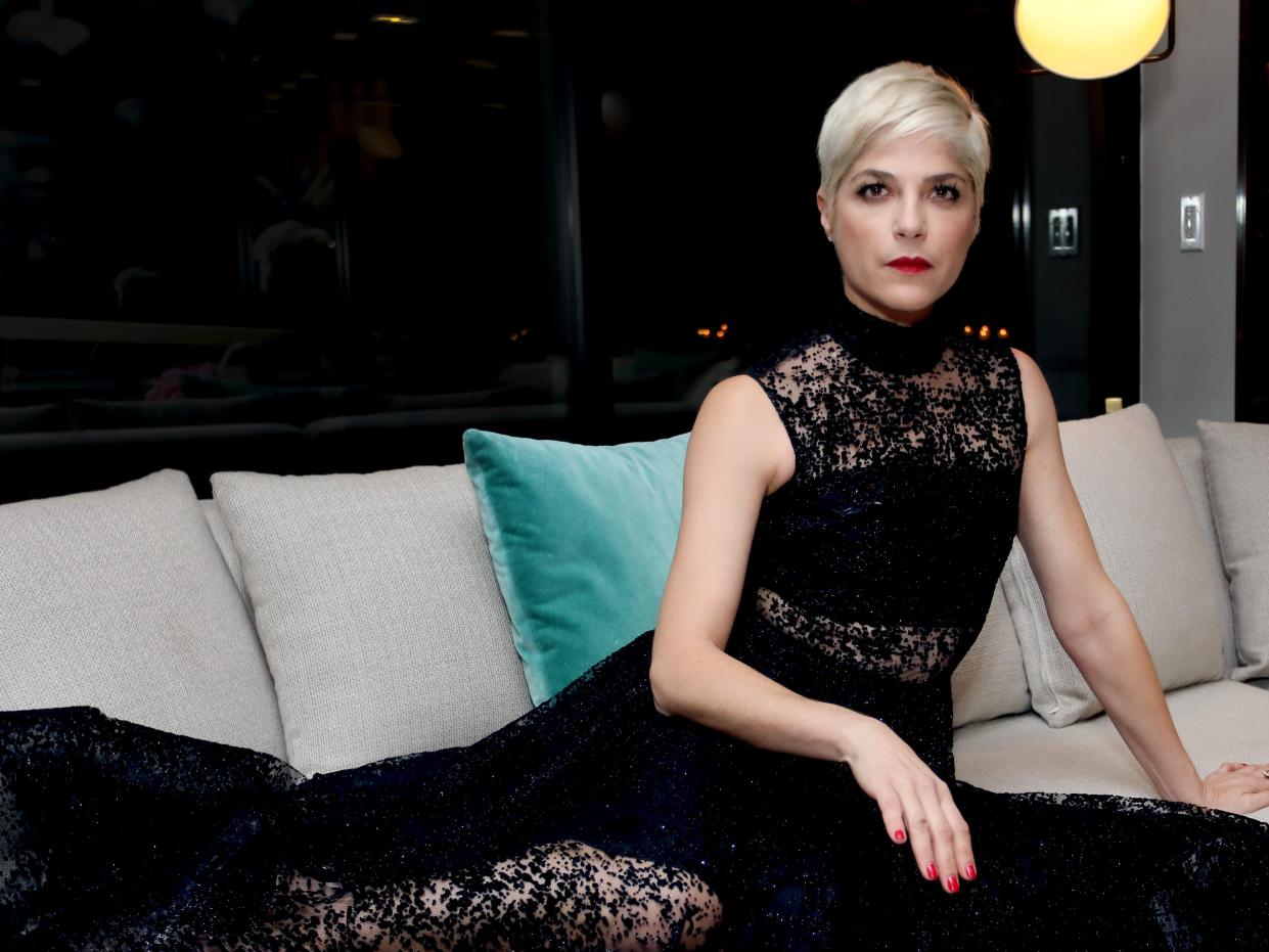 Selma Blair sits on a couch in a black dress.