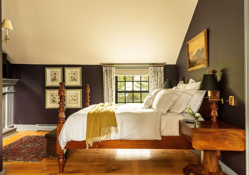 A plush white bed sits on a wood frame above an Oriental rug at the Weston hotel, Vermont