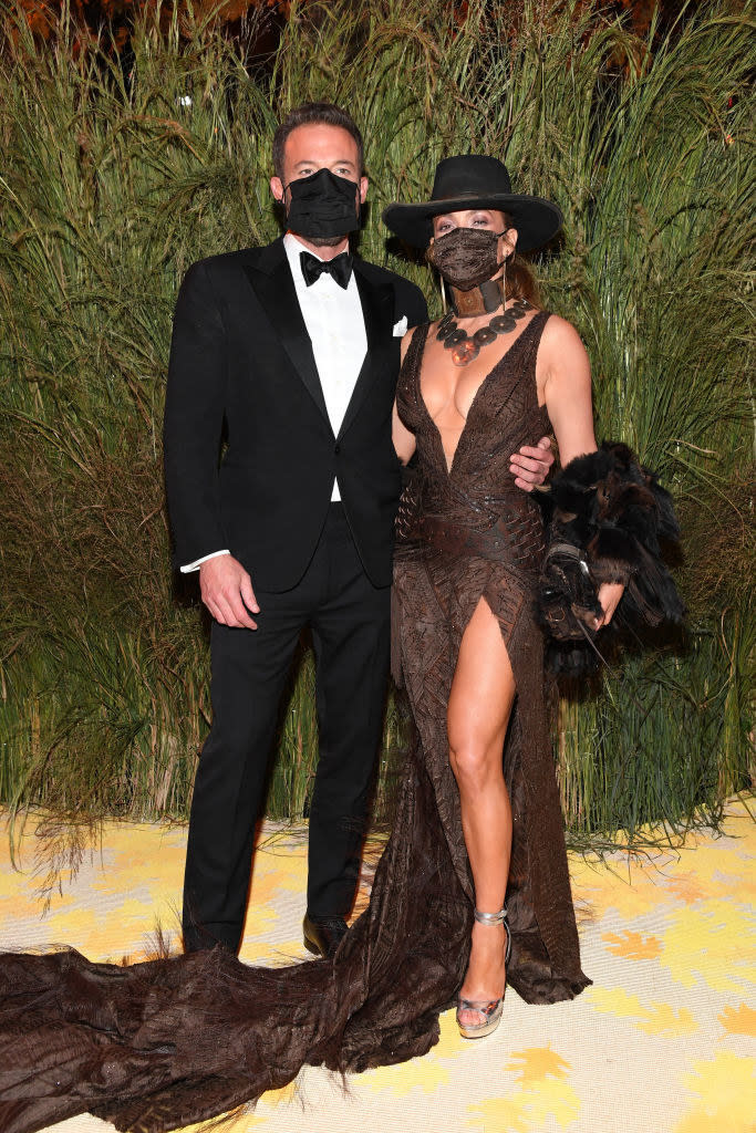 Ben Affleck wears a dark suit and Jennifer Lopez wears a floor length deep v-neck gown