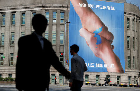 People walk past a large banner adorning the exterior of City Hall ahead of the upcoming summit between North and South Korea in Seoul, South Korea April 25, 2018. REUTERS/Jorge Silva