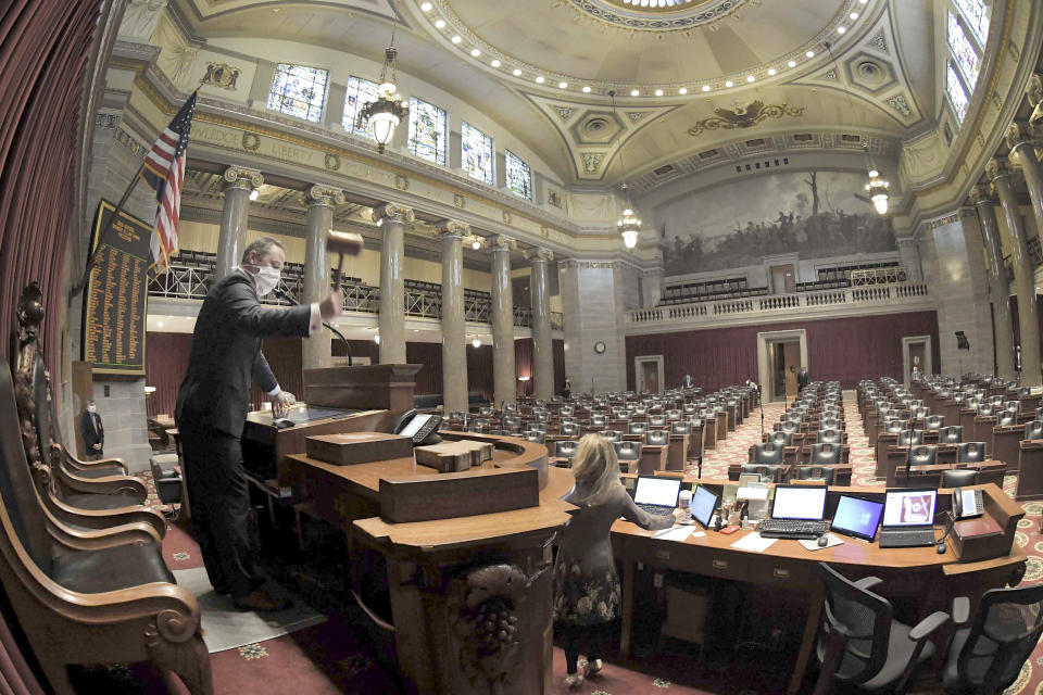 This April 8, 2020 file photo Missouri House Speaker Elijah Haahr wears a protective mask as he lowers the gavel in a nearly empty chamber to open the session in Jefferson City, Missouri. Some state lawmakers are having to choose between risking their health and carrying out their elected duties amid the coronavirus outbreak. Over the past month, at least 13 states have approved some form of remote voting for lawmakers in at least one of their legislative chambers, but others are pressing ahead with in-person sessions to vote on spending and other hot topics. (Tim Bommel/Missouri House of Representatives via AP)