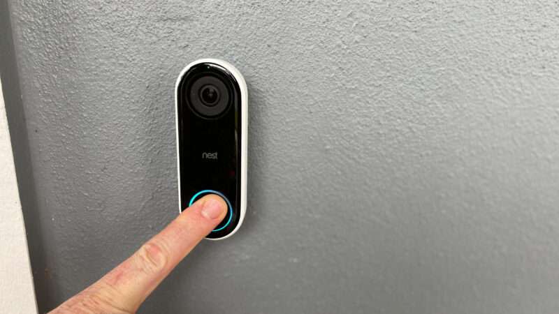 An outstretched hand presses the button on a Ring video doorbell.