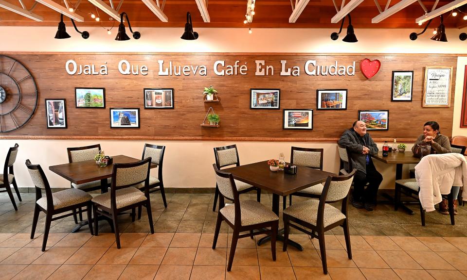 Maritza Reyes of West Boylston and her father, Juan Reyes, of Worcester wait for their food at La Central Bakery & Cafe. The inscription on the wall translates to, "We hope it rains coffee in the city."
