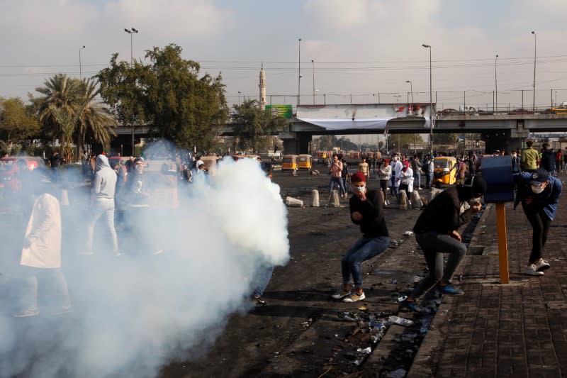 An Iraqi demonstrator runs as he carries a tear-gas canister to throw back during ongoing anti-government protests, in Baghdad