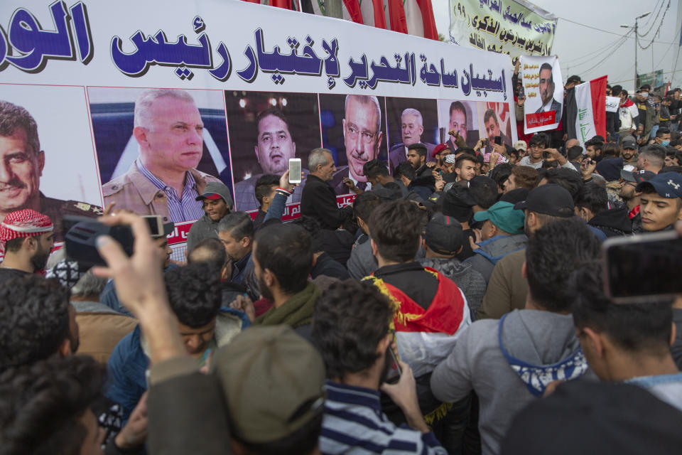 Anti government Iraqi protesters gather by a banner with pictures of Iraqi politicians and Arabic that reads "the Tahrir square questionnaire to select a prime minister," during the ongoing protests in Tahrir square, Baghdad, Iraq, Friday, Jan. 10, 2020. (AP Photo/Nasser Nasser)