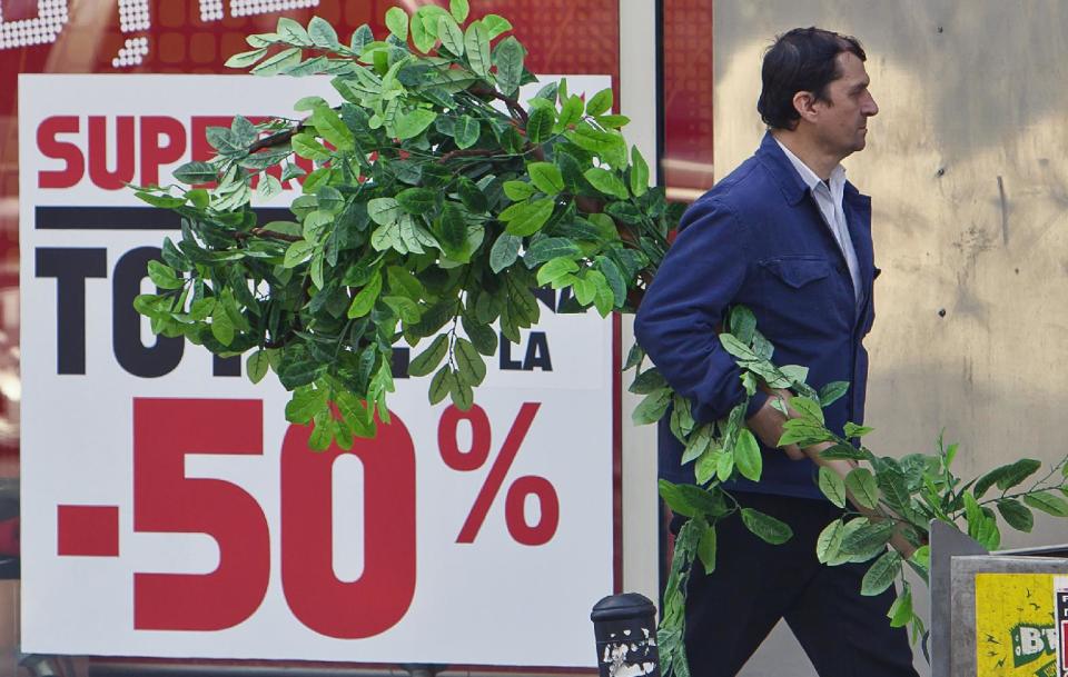 A man carries an artificial plant in Bucharest, Romania, back dropped by a shop window advertising price reductions for sports equipment, Monday, March 19, 2012. The coldest winter in living memory is over, and spring has arrived in Prague, Belgrade and Bucharest, but from the look in shop windows, with massive reductions and bargains galore, you'd think we were still in the winter sales. (AP Photo/Vadim Ghirda)