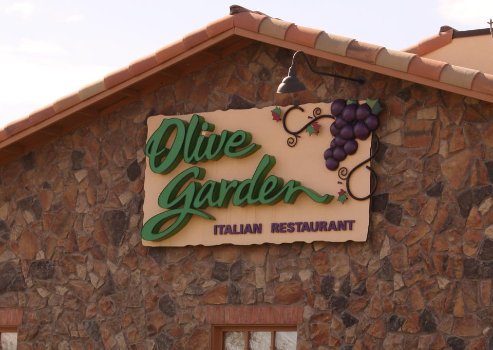 "Westminster, U.S.A.  -- April 30, 2012:  Olive Garden sign on the exterior of a restaurant, the background is stone.  The Olive Garden sign has 'Olive Garden' in large green letters, 'Italian Restaurant' in deep purple, and grapes in the right corner."