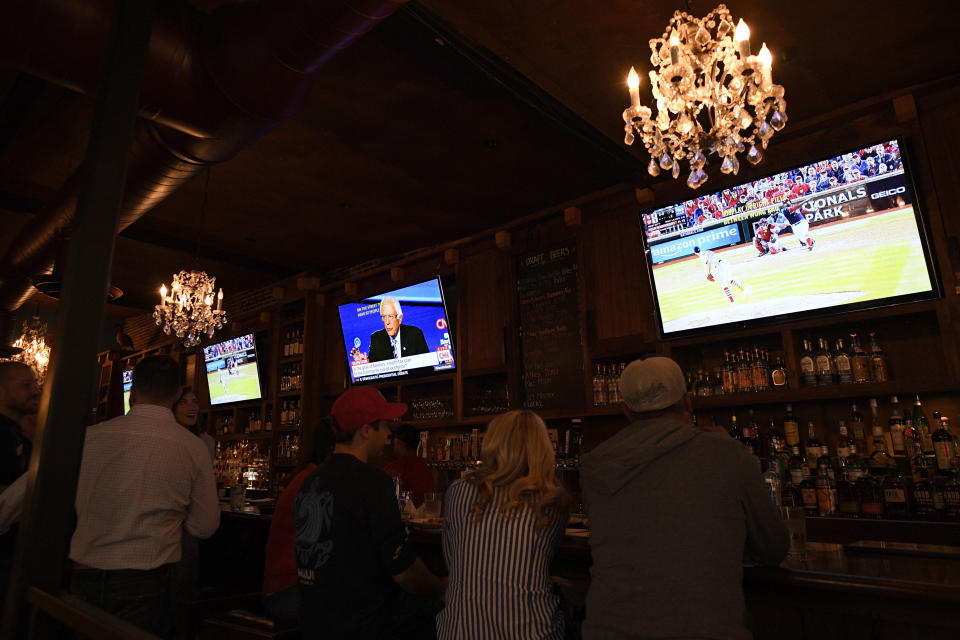 Patrons at the Hawk 'n' Dove sit in front of television screens televising Game 4 of the NLCS between Washington Nationals and the St. Louis Cardinals and a debate by Democratic presidential candidates, Tuesday, Oct. 15, 2019, in Washington. (AP Photo/Nick Wass)