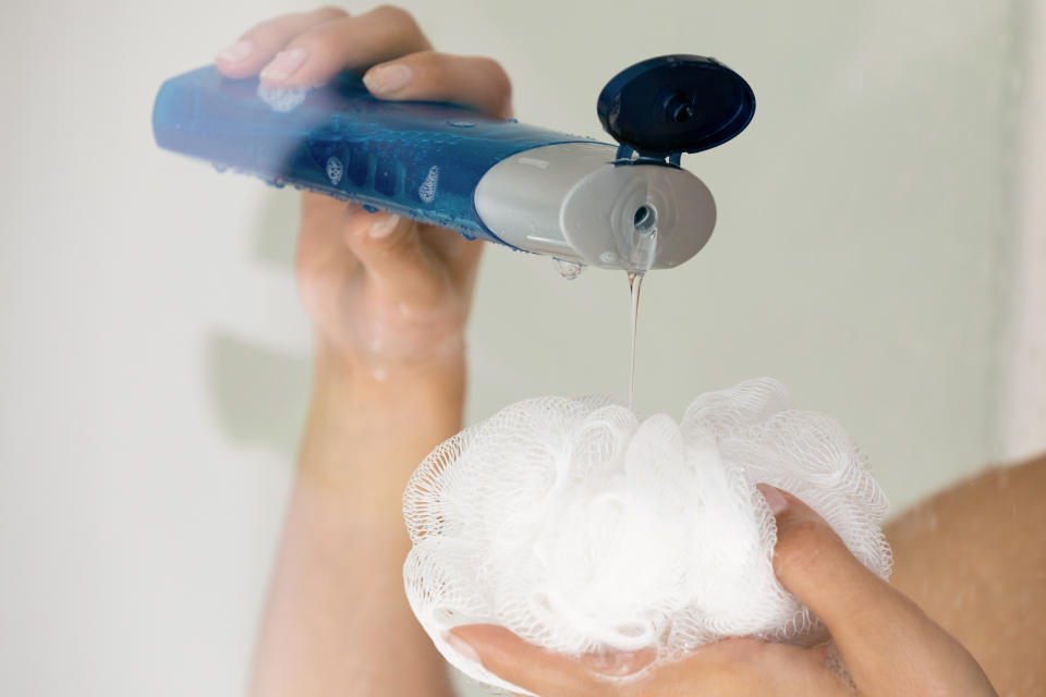 Close up young woman pouring liquid moisturizing soap shower gel from cosmetic bottle on loofah puff